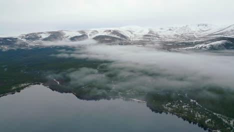 Volando-A-Través-De-La-Niebla-Sobre-Un-Lago-Con-Aspecto-De-Cristal-Hacia-Montañas-Cubiertas-De-Nieve.