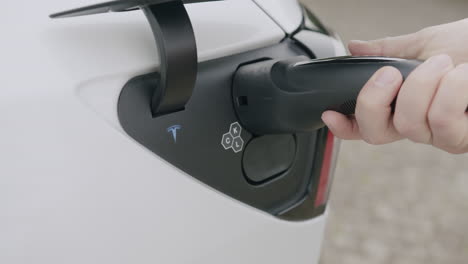 Tesla-driver-puts-the-charging-plug-into-the-charging-port-close-up
