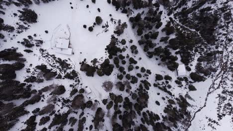 Aerial-top-down-winter-snow-covered-mountain-slope,-trees-glowing-and-snowy-hut-cabin-Lehnberghaus-in-Austria