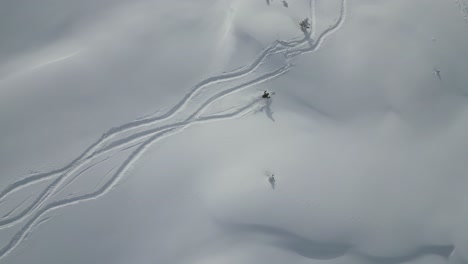 Aerial-following-young-sports-man-skiing-down-snow-covered-glacier-mountain-range-slope-in-snowy-alpine-scenery,-top-down-view