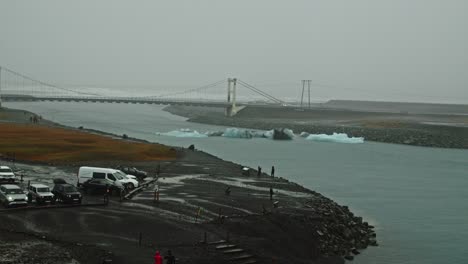 Wide-view-of-the-Jokulsarlon-lagoon-with-icebergs-on-the-water-and-a-bridge-in-the-distance