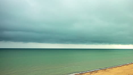 Timelapse-shot-of-dark-cloud-moving-over-sandy-beach-with-sea-waves-crashing-on-a-rainy-day
