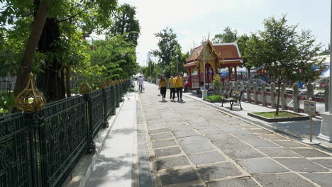 Turistas-Y-Fieles-Caminan-Por-Una-Calle-Estrecha-Junto-A-Un-Templo-Comunitario-En-Una-Aldea-Local-En-Bangkok,-Tailandia