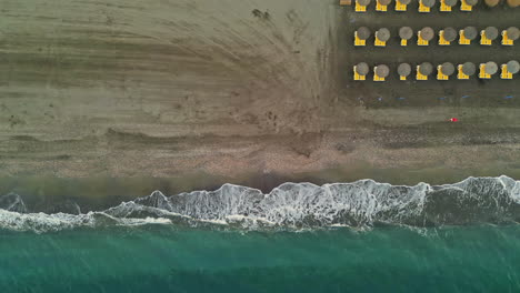 Eine-Luftaufnahme-Von-Meereswellen,-Die-Mit-Sonnenschirmen-In-Spanien-Zum-Strand-Strömen