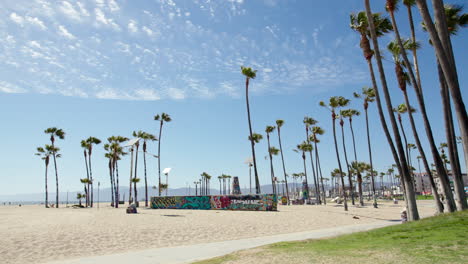 Wide-shot-of-Venice-Beach-and-bike-path-with-palm-trees-and-cyclists-biking-on-the-path