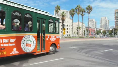 Colourful-tour-bus-loaded-with-tourists-on-the-street-of-Downtown-San-Diego-with-palm-trees-and-buildings