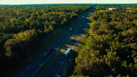 great-motorway-surrounded-by-plenty-high-trees-semi-trucks-and-personal-cars-traveling-across-long-roads-opposite-directions-vivid-saturated-colours-horizon-between-earth-and-sky-cinematic-drone-view
