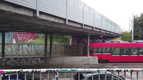 Ein-Roter-Straßenbahnwagen-Fährt-Unter-Einer-Brückenstraße-Mit-Graties-In-Bern-In-Der-Schweiz-Hindurch