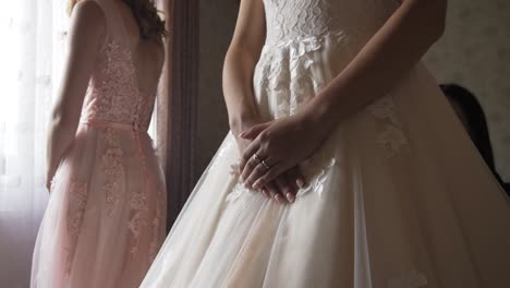 Close-up-of-Bride-holding-hands-over-vintage-dress-and-bridesmaid-standing