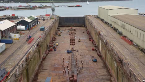 Big-empty-dry-dock-in-Falmouth-shipyard,-with-industrial-equipment-and-cranes-for-shipbuilding
