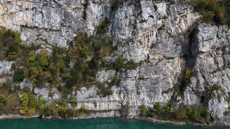 Ascending-drone-shot-of-steep-cliff-face-wall-and-blue-swiss-Walensee-Lake-Walen-with-trees