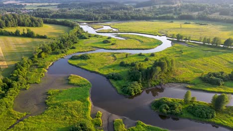 Filmische-Drohnenansicht-Eines-Blauen-Flusses,-Der-Durch-Eine-Grüne-Landschaft-Auf-Dem-Land-Fließt