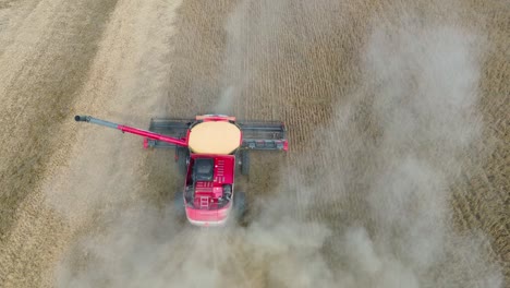 Farm-Combine-harvesting-soybeans-with-trailed-by-a-dust-cloud-on-a-Midwestern-farm,-aerial-drone