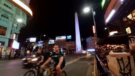 POV-view-of-obelisk-in-Buenos-Aires-city-with-young-people-riding-bicycles-and-traffic-jam,-Argentina