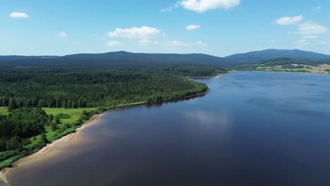 cinematic-drone-view-of-a-blue-lake-and-a-large-green-forest-that-stretches-right-next-to-the-lake