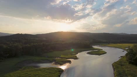 cinematic-view-from-a-drone-of-sunset,-when-flying-over-a-river-that-flows-through-a-green-countryside-in-the-countryside