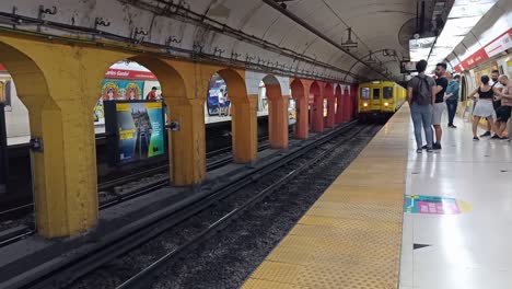 Metro-Llegando-A-La-Estación-De-Metro-Mientras-Los-Pasajeros-Esperan-En-La-Ciudad-De-Buenos-Aires,-Argentina