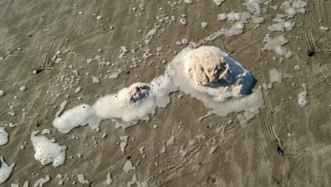 Dirty-beach-foam-froth-slowly-moving-across-sandy-Welsh-sand-with-tide-waves