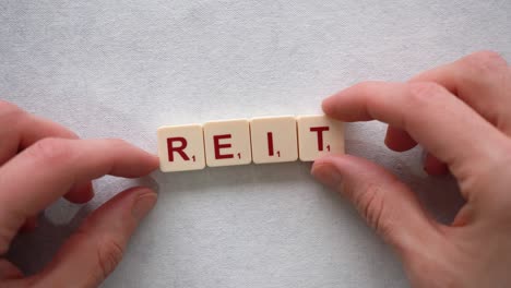Human-hands-creating-the-word-"REIT"-with-red-letters