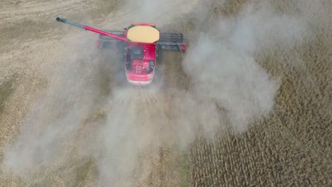 Farm-Combine-harvesting-soybeans-with-trailed-by-a-dust-cloud-on-a-Midwestern-farm,-aerial-drone