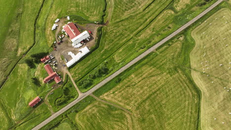 Toma-Aérea-Superior-Sobre-Una-Carretera-Con-Campos-Verdes-Y-Una-Casa-De-Granjero-En-Islandia