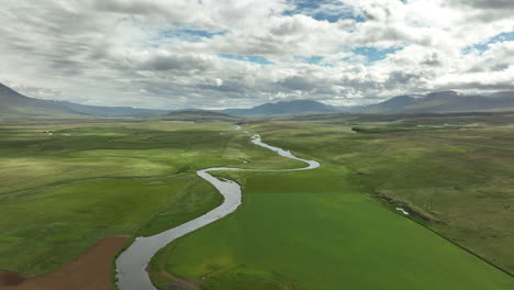 Río-En-Islandia-Que-Fluye-En-Tierras-De-Cultivo-Toma-Aérea-Día-Nublado-Con-Montañas