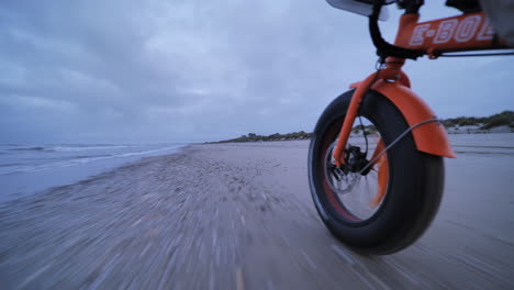 Man-cycling-on-a-beach-close-wheel-shot-orange-electric-bike-France-Occitanie