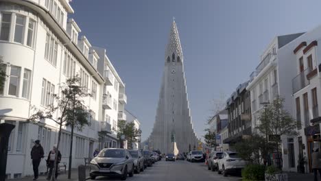 Busy-city-street-filled-with-cars-and-pedestrians-walking,-view-of-the-Hallgrimskirkja-church-in-Iceland