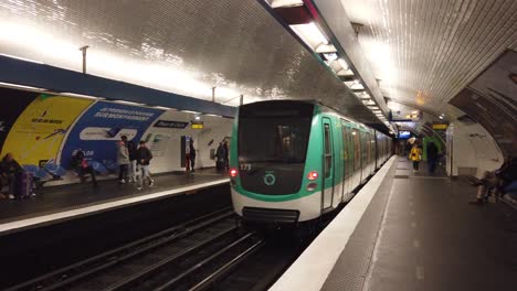 Un-Transporte-En-Tren-Del-Metro-De-París-Sale-Dentro-De-La-Estación-Place-De-Clichy,-Francia,-Con-Gente-Caminando