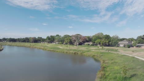 Aerial-drone-view-of-a-female-cyclist-with-a-child-carrier-bike-riding-on-the-Exploration-Green-Recreation-path-under-blue-skies-and-white-clouds-in-Clear-Lake,-Houston,-Texas