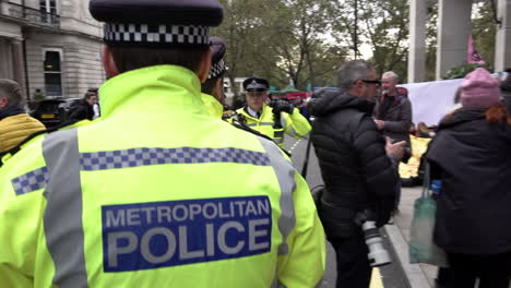 A-unit-of-Metropolitan-police-officers-wearing-yellow-reflective-jackets-walk-into-a-crowd-of-Extinction-Rebellion-climate-change-protestors,-stop-and-listen-to-the-instructions-from-a-senior-officer