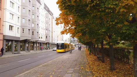 Herbstsaison-In-Berlin-Mit-Gelber-Straßenbahn,-Die-An-Einem-Bunten-Baum-Vorbeifährt,-Deutschland