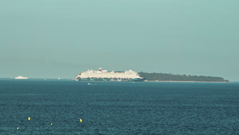 Cruise-ship-sails-past-Sainte-Marguerite,-Cannes-backdrop.