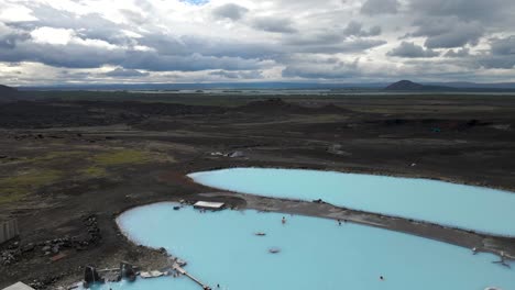 Revel-in-aerial-tranquility-over-Mývatn-Nature-Baths,-where-deep-blue-hot-pools-offer-a-serene-contrast-to-Lake-Mývatn's-expanse-in-vivid-4K