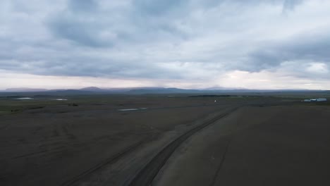 Under-an-overcast-sky,-a-4K-drone-captures-Iceland's-raw-terrain,-featuring-a-stark-landing-strip-with-majestic-mountains-looming-in-the-backdrop