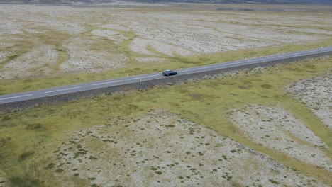 Traverse-Iceland's-scenic-expanses-with-this-captivating-4K-drone-footage,-featuring-a-unique-arial-view-as-a-car-drives-through-the-bare-countryside-of-Iceland