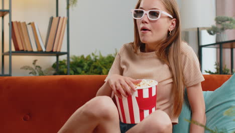 Woman-sitting-on-couch-eating-popcorn-and-watching-interesting-TV-3D-film,-sport-game-online-at-home