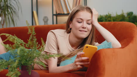 Young-woman-lying-on-sofa-at-home,-using-smartphone-share-messages-on-social-media-application
