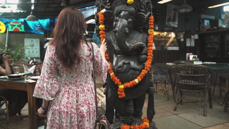 An-Indian-woman-fully-embracing-the-local-culture-while-seated-in-a-traditional-local-bar,-gently-caressing-a-sculpture-of-Ganesha-in-Panaji,-Goa,-India-on-31-08-2023