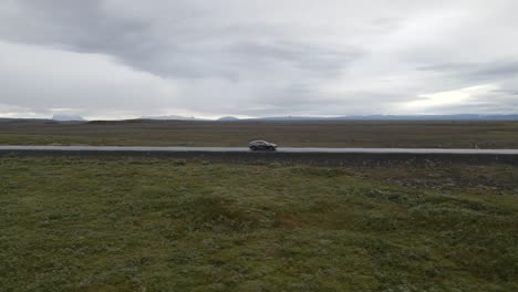 Fahren-Sie-Mit-Einem-Auto-Durch-Die-Weiten-Ebenen-Islands-Und-Folgen-Sie-Einem-Auto-Mit-Einer-4K-Drohne-Durch-Endlosen-Dreck-Und-Ferne-Berge