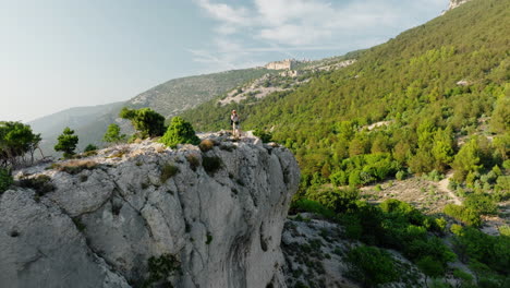 Adventurer-stands-at-white-cliff-edge-as-drone-pullsback-on-Lubenice-Cres-Croatia