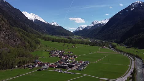 Picturesque-mountain-village-in-green-valley-between-steep-alpine-mountains,-aerial