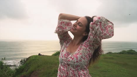 A-young-Indian-girl-radiating-happiness-as-she-smiles-on-a-vibrant-green-field-with-the-sea-in-the-background,-wearing-a-beautiful-floral-dress-of-liberty-in-Panaji,-Goa,-India-on-31-08-2023