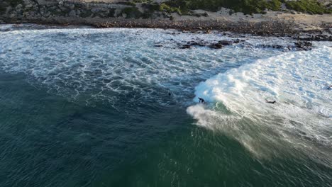 Surfer-riding-the-waves-near-the-seashore-at-sunset-in-Gracetown,-Western-Australia,-aerial-tracking-shot