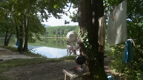 Off-grid-camping-scene-near-to-lake-with-personal-items-hung-on-trees