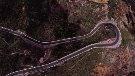 Winding-serpentine-road-with-cars-driving-during-evening-glden-hour-in-rocky-terrain,-Aerial-top-down,-Tenerife