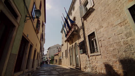 Blue-flags-wave-in-wind-from-balcony-of-historic-stone-building-in-Cres,-Croatia