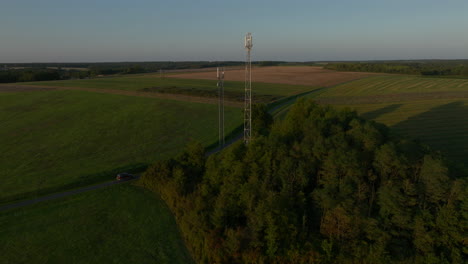 Two-cellular-towers-in-the-middle-of-farmland-during-sunrise,-aerial-dolly-out-tilting