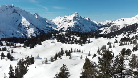 Vista-Por-Drones-De-Esquiadores-Disfrutando-De-Las-Cadenas-Montañosas-Cubiertas-De-Nieve-En-Warth,-Un-Pequeño-Municipio-En-Vorarlberg,-Austria-En-4k