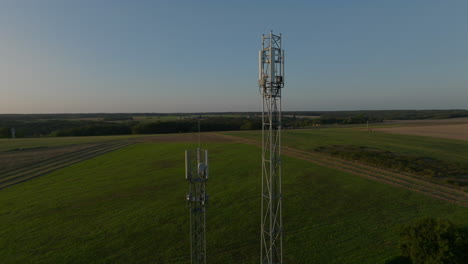 Two-cellular-towers-in-the-middle-of-farmland-during-sunrise,-aerial-orbital